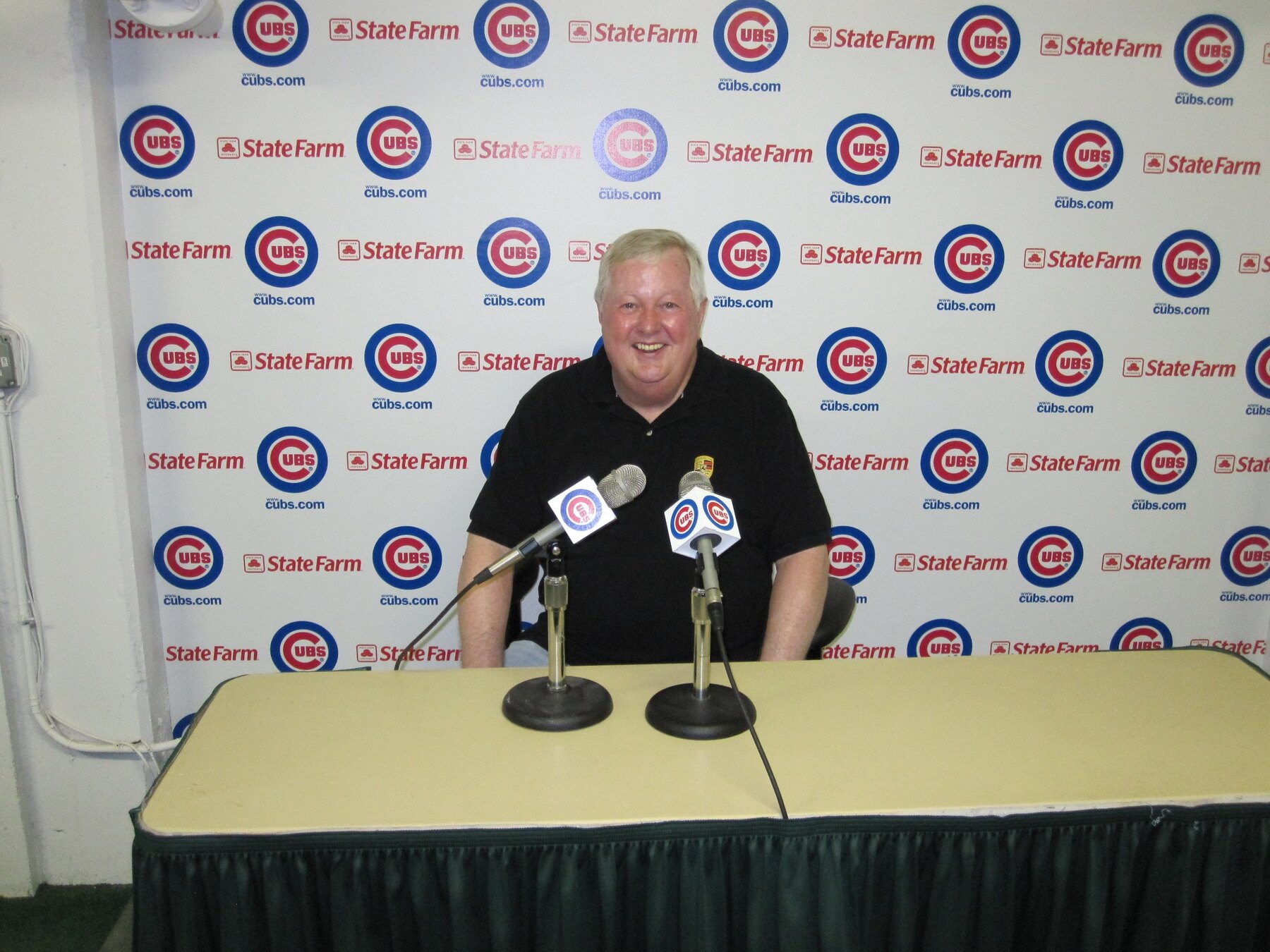 Tom Snyder smiling behind microphones at a Chicago Cubs backdrop